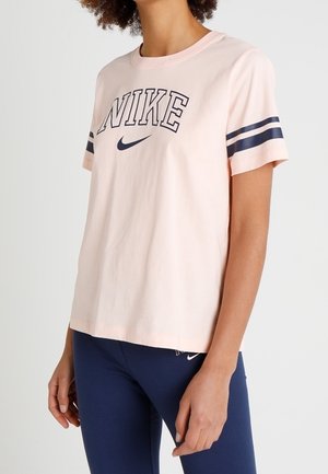 Kvinde iført en lyserød Nike t-shirt med marineblå striber på ærmerne og marineblå leggings med et lille Nike-logo.