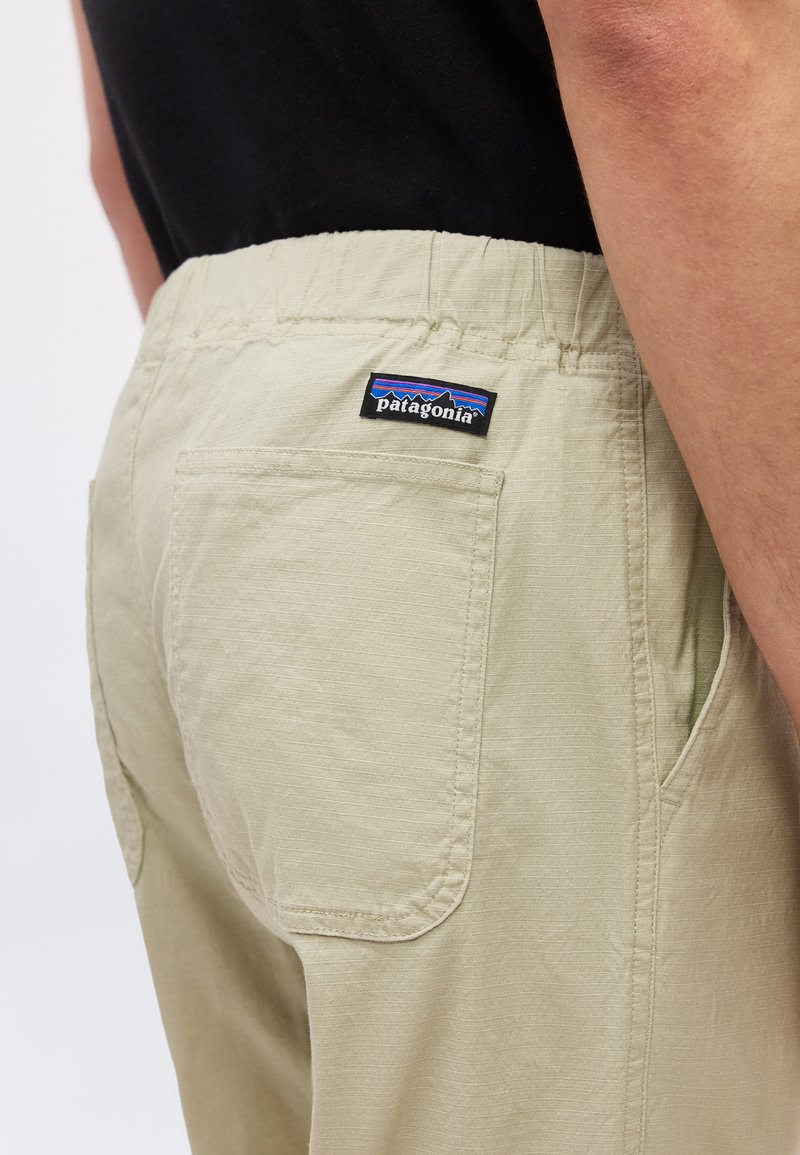 Beige pants with back pocket and Patagonia brand label worn by person in black shirt, shown from waist to mid-thigh.