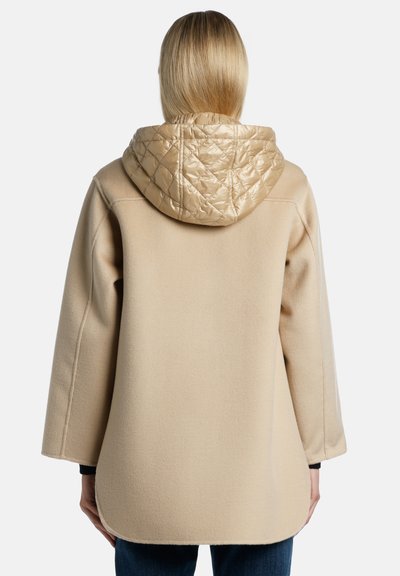 Cappotto in misto lana beige con cappuccio trapuntato beige, vestibilità rilassata, spalle cadute e orlo curvo, che mette in mostra morbidezza e design strutturato.