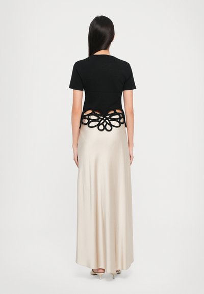 Black short-sleeve top with cut-out floral design at the back, paired with a long beige silk skirt; minimal hardware, smooth texture.