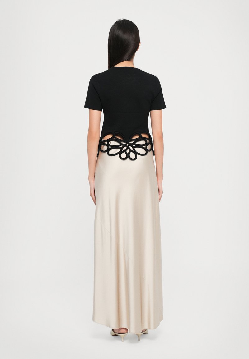 Haut noir à manches courtes avec un design floral découpé à l'arrière, associé à une longue jupe en soie beige ; matériel minimal, texture lisse.