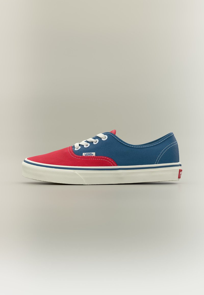 Baskets Vans basses avec l'avant rouge, les côtés bleus, des lacets blancs et une semelle en caoutchouc blanche, vues de profil sur un fond uni.