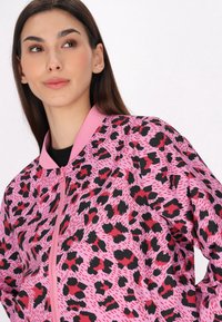 Giacca bomber rosa con stampa leopardata nera e rossa, con colletto e chiusura a zip in contrasto di colore rosa solidale. Tessuto dalla superficie liscia.
