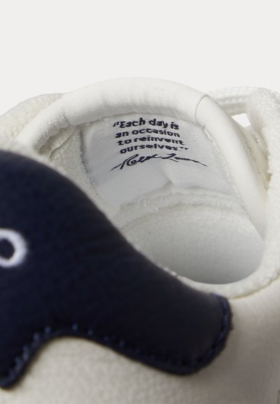 Εσωτερικό λευκού αθλητικού παπουτσιού με μαύρο κείμενο στη γλώσσα που γράφει, «Κάθε μέρα είναι μια ευκαιρία να ξαναδημιουργήσουμε τον εαυτό μας», και μια υπογραφή από κάτω.