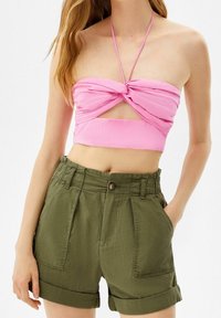 Rosa croppad topp med en vriden design och halterneck, matchad med högmidjade, gröna linne-shorts med framfickor och rullade cuffs.
