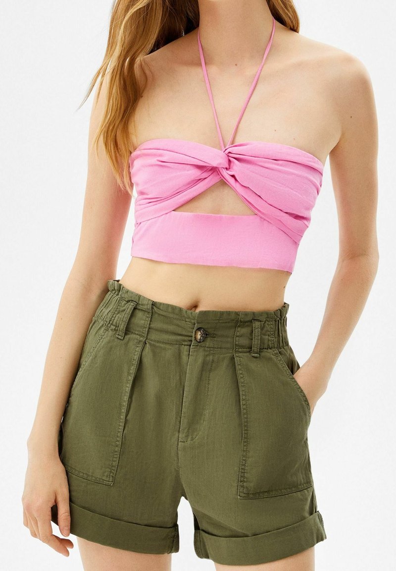 Rosa croppad topp med en vriden design och halterneck, matchad med högmidjade, gröna linne-shorts med framfickor och rullade cuffs.