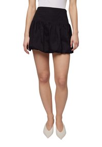 Gonna corta nera realizzata in un tessuto texturizzato, con vita aderente e design arricciato e voluminoso. Abbinata a tacchi bianchi a punta.