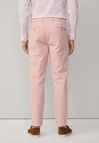 Pantaloni rosa chiaro con due tasche posteriori dotate di bottoni, realizzati in cotone, abbinati a scarpe slip-on marroni.