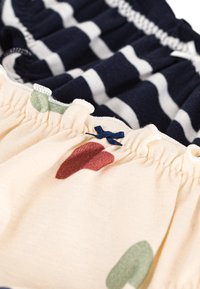 Deux morceaux de tissu : l'un marine avec des rayures blanches, l'autre crème avec des pois colorés et un accent en nœud marine. Bords doux et froncés.