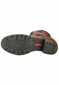Bota de cuero marrón con suela de goma negra texturizada, que presenta profundos tacos, marca roja y acentos de hardware plateado.