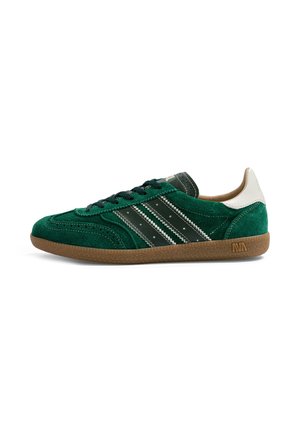 Baskets en daim vert avec des rayures noires et blanches, lacets noirs, languette blanche au talon, semelle marron avec une accroche texturée et petit logo.