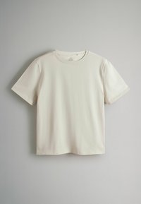 T-shirt simple à manches courtes et col rond de couleur blanc cassé suspendu devant un fond gris clair, montrant la vue de face sans logos ni motifs visibles.