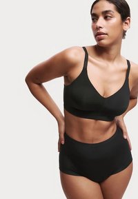 Zwarte bralette met een V-hals ontwerp en verstelbare bandjes, gecombineerd met hoog getailleerd zwarte ondergoed, beide gemaakt van een gladde, zachte stof.
