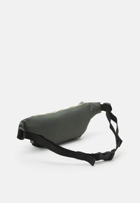 Borsa in tessuto verde con cinturino nero, dotata di un comparto con zip e un accento giallo lungo la zip, texture morbida e forma ergonomica.