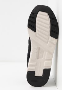 Semelle de basket noire avec une adhérence en caoutchouc texturé, dotée d'une semelle intermédiaire blanche et d'un logo de marque embossé. Design plat avec un motif de bande de roulement défini.