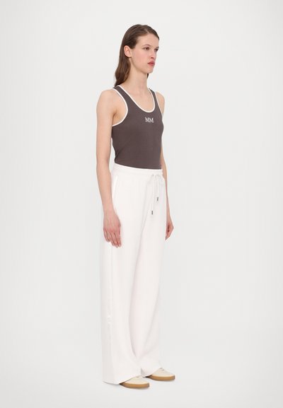 Brūns ribots topiņš ar baltu apmalīti un "MM" logotipu; apvienots ar brīvām baltām biksēm ar auklu un sānu vīlēm.