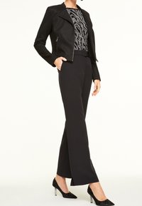 Veste noire ajustée avec un haut à motif animal texturé, associée à un pantalon noir sur mesure. Chaussures à talons hauts noires avec un accent réfléchissant.