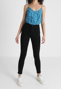 Blå djurmönstrad linne-topp med tunna band, kombinerad med höga svarta tajta jeans och vita sneakers. Mjukt tyg, figurnära design.