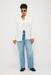 White linen button-up shirt over a white tank top, paired with light blue ripped jeans and black chunky boots, accessorized with round sunglasses.