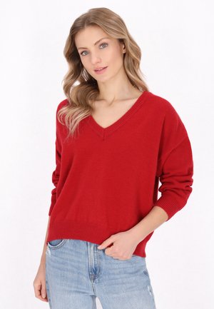 Maglione rosso a maglia con scollo a V, maniche lunghe e polsini a coste. Abbinato a jeans chiari strappati. Tessuto morbido, vestibilità rilassata.
