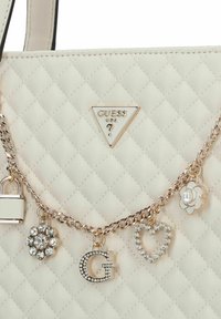 Gepinster Handtasche in Creme mit metallischer Kettenriemen, verziert mit Charms: einem Schloss, einer Blume, einem Herzen, floralen Designs und dem eingearbeiteten Buchstaben "G". Akzente aus Silberhardware.