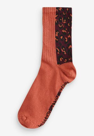 Chaussette orange avec texture côtelée et une section sombre bourgogne à motifs présentant un design d'imprimé animal. Détails de orteil et de talon renforcés.