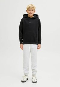 Felpa nera con cappuccio e tasca frontale, pantaloni tuta grigi e sneakers bianche con dettagli neri. Un outfit semplice e casual.