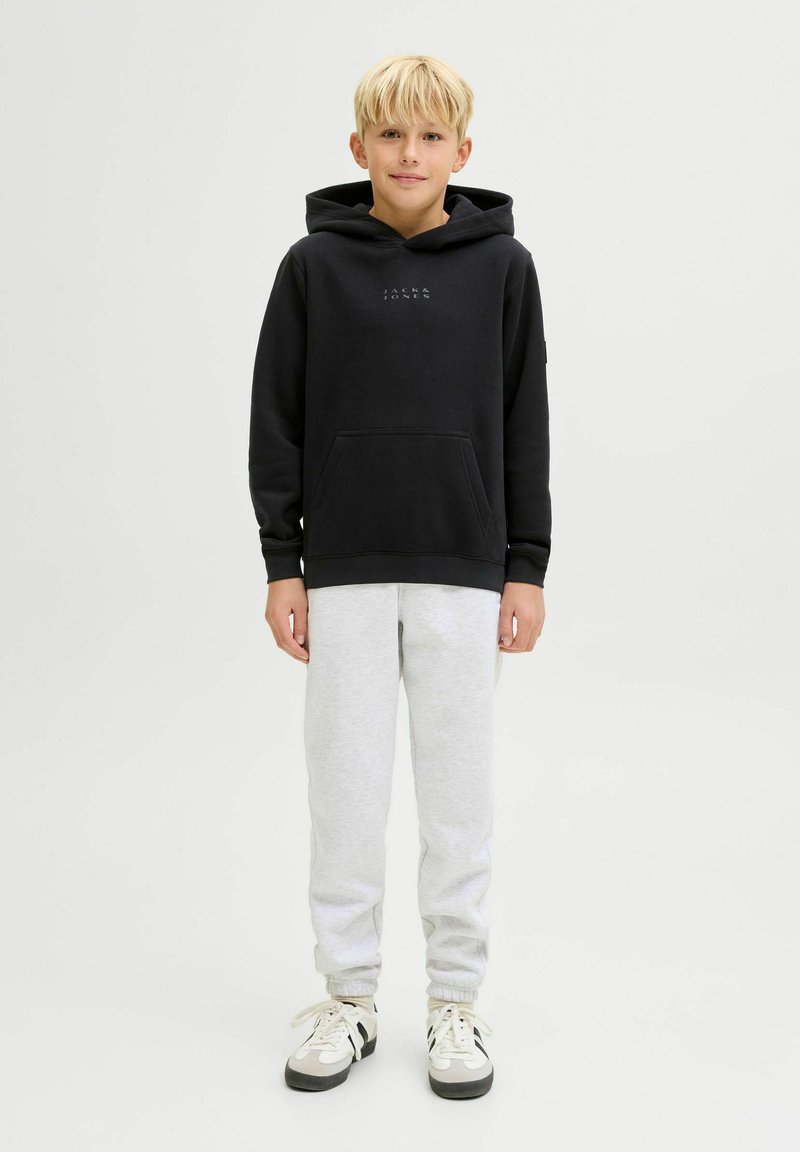 Felpa nera con cappuccio e tasca frontale, pantaloni tuta grigi e sneakers bianche con dettagli neri. Un outfit semplice e casual.