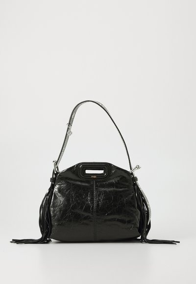 Black glossy leather handbag with a top handle and shoulder strap, featuring side tassels and a small cutout grip at the top center.