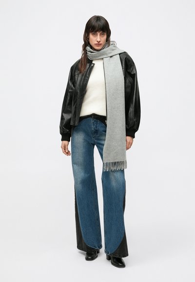 Μαύρο δερμάτινο bomber μπουφάν, λευκό πουλόβερ, γκρι κασκόλ με φουντίτσες, φαρδύ μπλε τζιν με μαύρες πινελιές, μαύρα μποτάκια στον αστράγαλο.