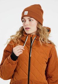Oranžová prešívaná bunda so zipsom, čierne akcenty, rebrované rukávy a zodpovedajúca čiapka s logom.