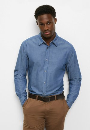 Hellblaues Hemd mit langen Ärmeln und Knopfleiste, mit dezentem Muster, ausgestelltem Kragen und abgerundeten Manschetten, kombiniert mit braunen Hosen.