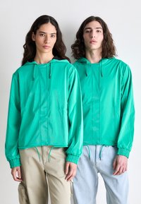 Jachete ușoare de culoare verde-bleu cu glugi, manșoane elastice și tiv cu șnur; textură netedă; design minimalist fără hardware vizibil.