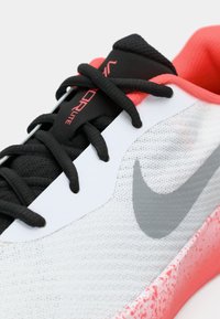 Nike superga s črno-belim mrežastim zgornjim delom, roza poudarki, gumijastim podplatom in izrazitim logotipom Swoosh. Ima črne vezalke in oblazinjen ovratnik.