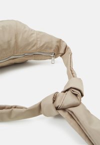 Beige vadderad handväska med en knuten handtag och en metallblixtlås. Materialet verkar slätt och något glansigt.