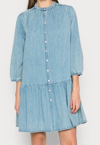 Ljusblå denimklänning med rund halsringning, trekvartslånga ärmar, knäppning fram, rynkad midja och utsvängd kjol.