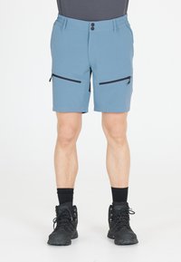 Blå stretchshorts med elastisk midja, två fickor med dragkedja på sidorna och en slät yta. Kombinerade med svarta vandringskängor och mörka strumpor.