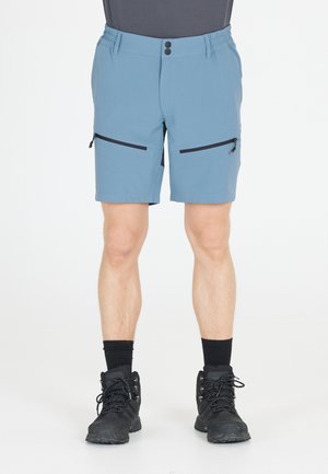 Blå strækshorts med elastisk talje, to lynlåslommer på siden og en glat tekstur. Kombineret med sorte vandrestøvler og mørke sokker.