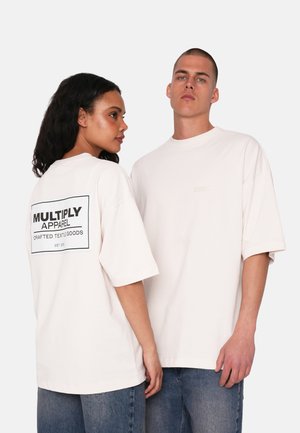 Camisetas de gran tamaño en color rosa con mangas cortas, que presentan un logo gráfico negro en la parte posterior y una pequeña etiqueta en la parte delantera, combinadas con denim.