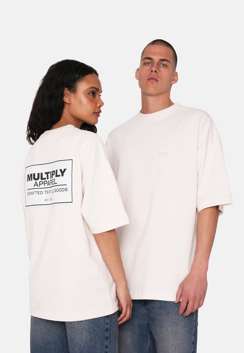 Camisetas de gran tamaño en color rosa con mangas cortas, que presentan un logo gráfico negro en la parte posterior y una pequeña etiqueta en la parte delantera, combinadas con denim.