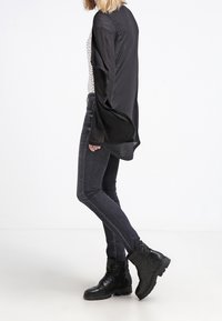 Maglietta nera a maniche lunghe con un design fluido, abbinata a jeans skinny grigi e stivaletti neri con lacci a caviglia con una finitura testurizzata.