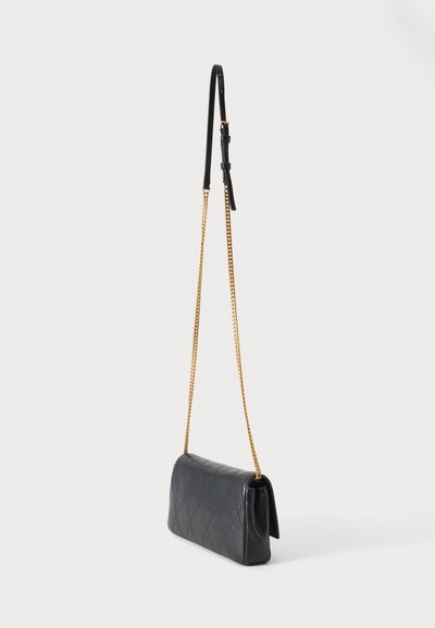 Μαύρη τσάντα crossbody από καπιτονέ δέρμα με χρυσή αλυσίδα και ρυθμιζόμενο μαύρο δερμάτινο λουρί ώμου σε απλό φόντο.