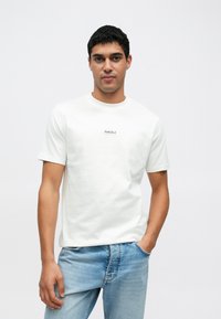 Valge puuvillane t-särk ümmarguse kaelusega ja lühikeste varrukatega, millel on rinnal väike must "Hust Club" logo. Kandmiseks sobivad hele sinised teksapüksid.