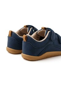 Des chaussures navy avec des bandes Velcro présentent un dessus lisse, des accents marron et une semelle en caoutchouc texturée pour une meilleure adhérence. Intérieur rembourré pour le confort.