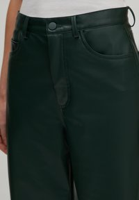 Groene neplederen broek met een gladde textuur, voorzakken, een knoopsluiting en een ontspannen pasvorm. Detailstiksel is zichtbaar.