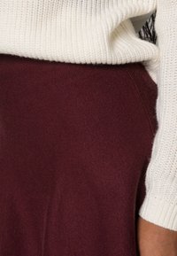 Cream ribbed knit sweater paired with a burgundy textured skirt, highlighting contrasting materials and warm tones.