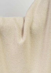 Beige strikket stof med en blød tekstur, der har en subtil glans og en glat overflade, der falder blødt og afslører sin fleksibilitet.