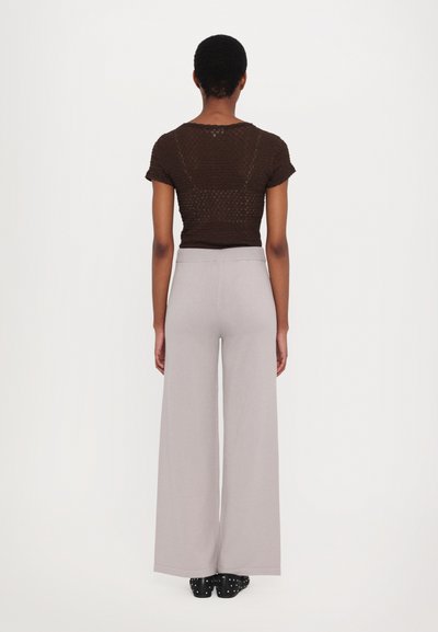 Brown short-sleeve top with textured pattern and gray wide-leg pants. Black shoes with white studs complete the outfit. Viewed from the back.