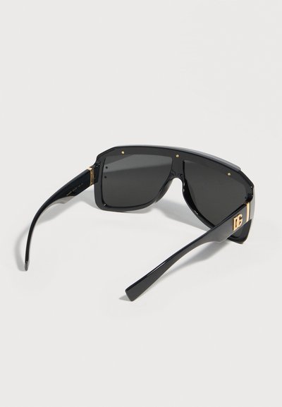 Μαύρα μεγάλα γυαλιά ηλίου με σκούρους φακούς, παχιά πλαίσια και χρυσά διακριτικά με το λογότυπο DG στους βραχίονες, πάνω σε λευκό φόντο.