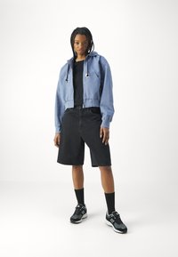 Kuttet blå hettegenser med glidelås, svart t-skjorte, svarte denimshorts, svarte sokker og svarte sneakers med hvite detaljer; avslappet passform, uformell stil.